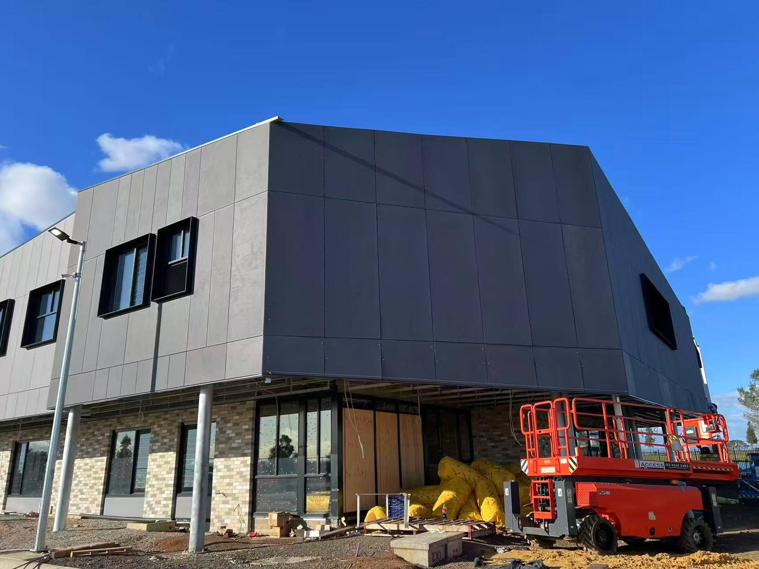 Two-storey building clad in dark fibre cement panels with expressed joints, above a brick ground floor