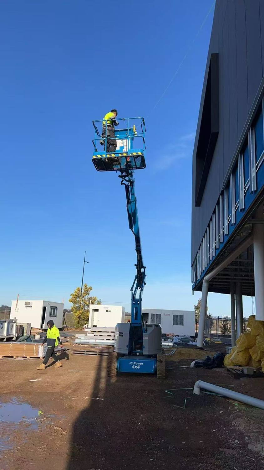 Installer on a boom lift working on a dark-clad façade